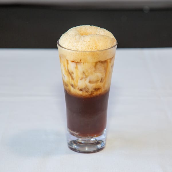 Tall glass with a dark beverage, creamy milk, and a thick layer of foam.