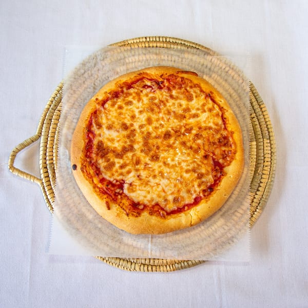 Round cheese pizza on a woven tray with parchment paper on a white tablecloth.