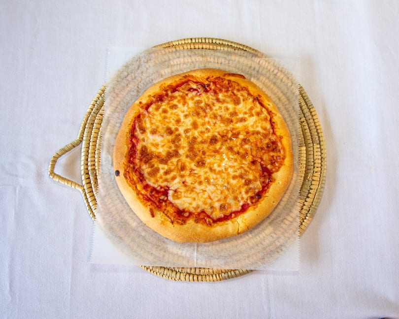 Round cheese pizza on a woven tray with parchment paper on a white tablecloth.