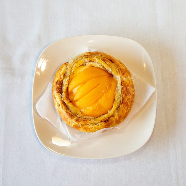 Round golden pastry with sliced peaches on a white plate and napkin.