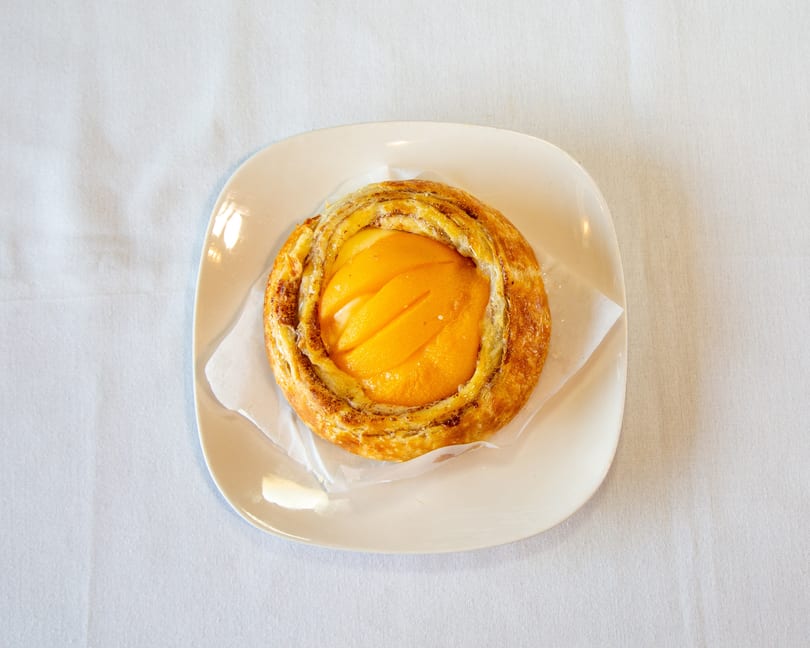 Round golden pastry with sliced peaches on a white plate and napkin.