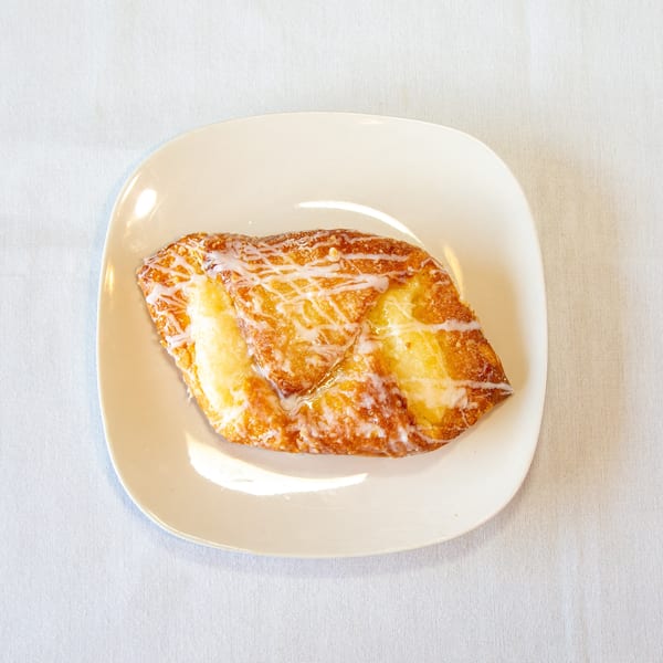 Golden-brown cheese Danish with white icing drizzle on a white plate.
