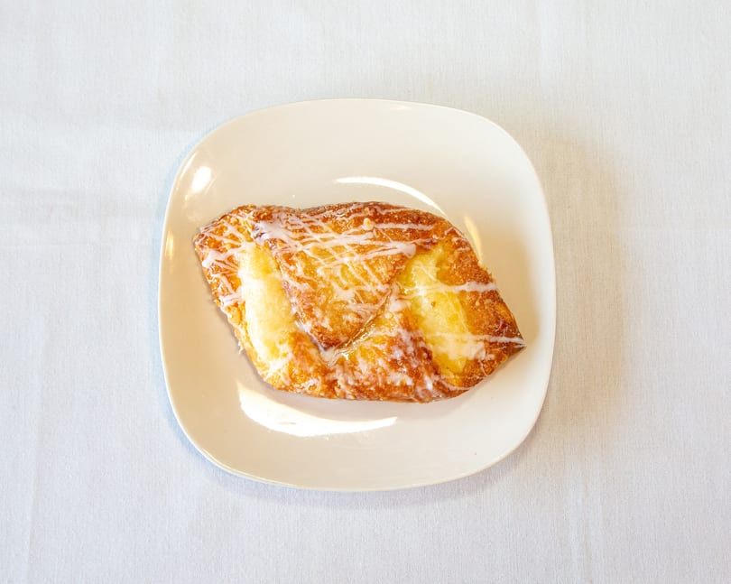 Golden-brown cheese Danish with white icing drizzle on a white plate.